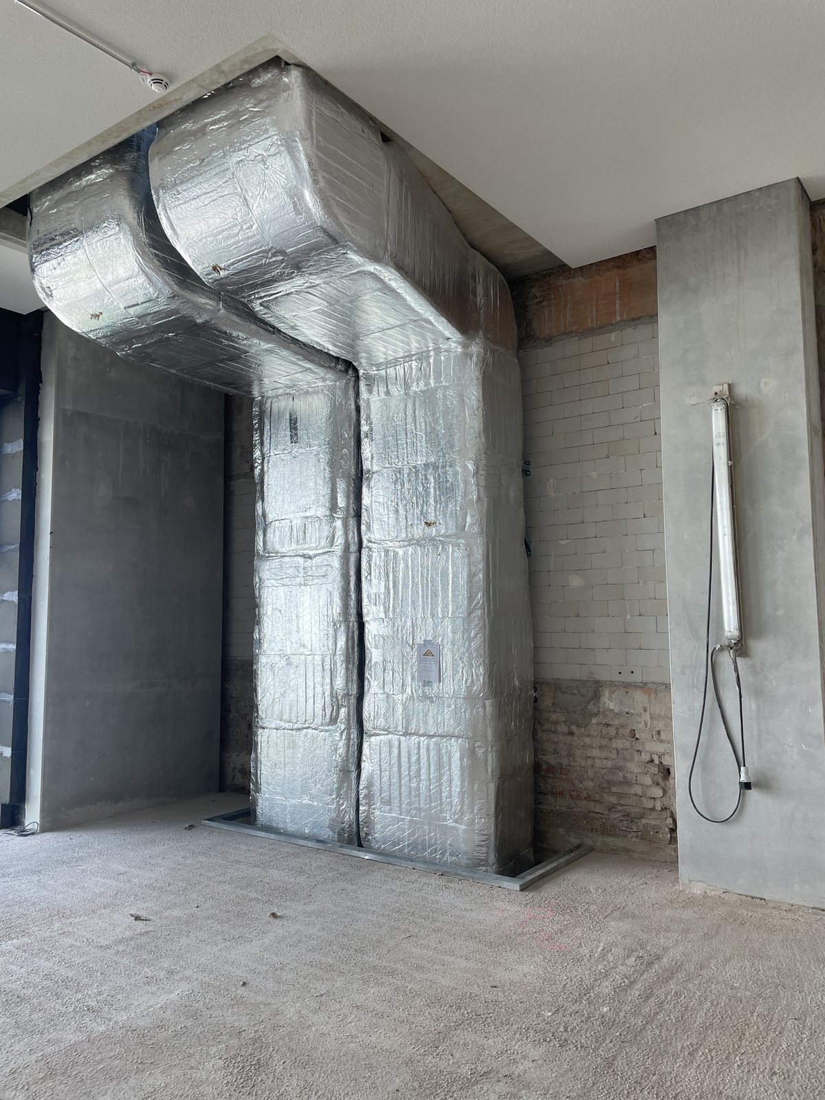 Zwei gedämmte Lüftungskanäle führen im Rohbau von der Decke an einer Wand herab